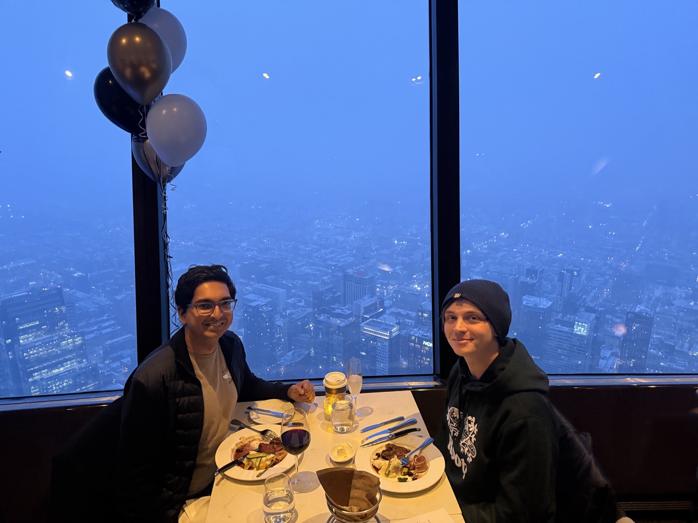 Cameron and Jamil at dinner atop the CN Tower, balloons overhead and Toronto's lights far below