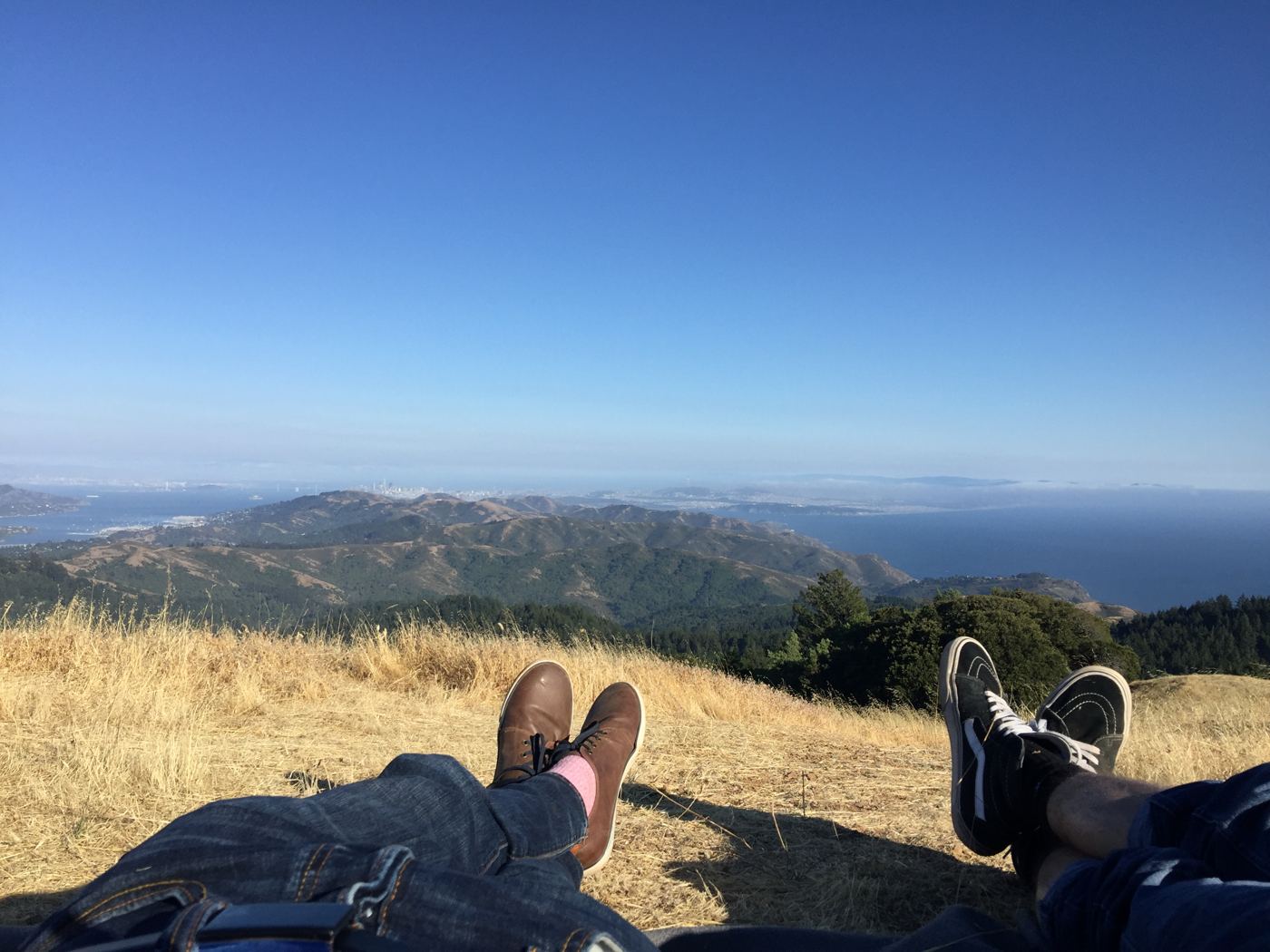 Two pairs of legs stretched out on the golden grass atop Mt. Tamalpais, San Francisco hazy across the bay