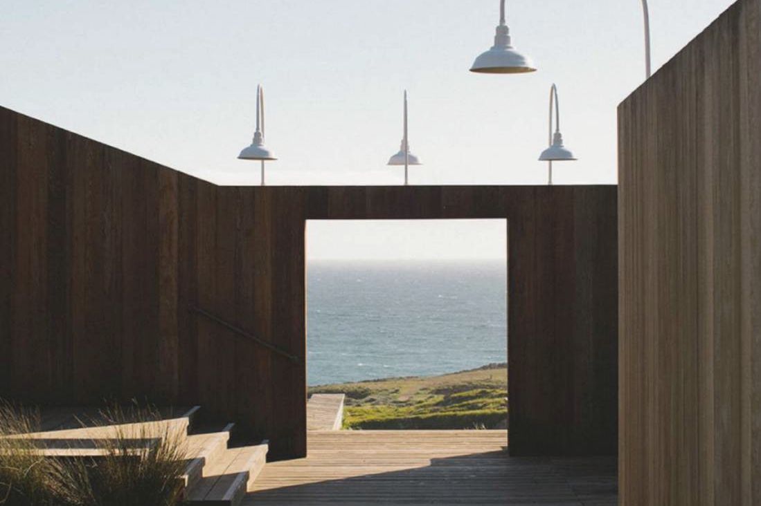 The Lodge's timber entry walls and boardwalk, gooseneck lamps above and the Pacific through the doorway